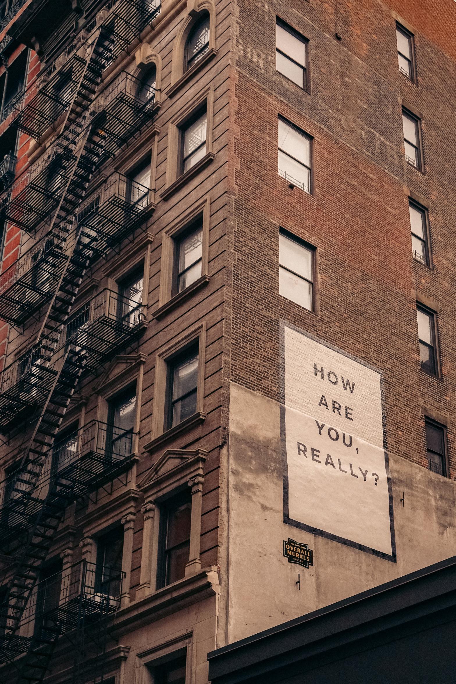 The side of a tall brick building with a painted mural asking, "How are you really?"